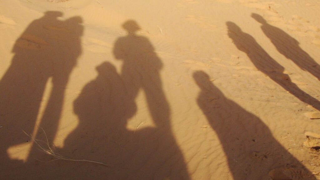 Lange Schatten von Reisenden fallen über die Sanddünen der Tadrart Rouge