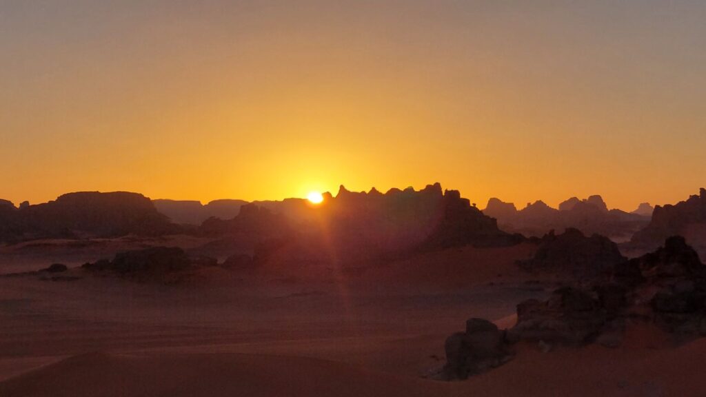 Sonnenuntergang über Felsformationen und Sanddünen in der Tadrart Rouge in Algerien
